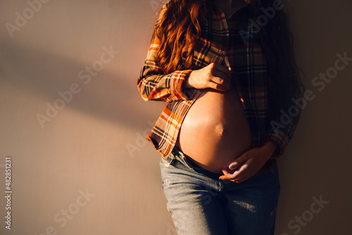 Pregnant woman, belly of a pregnant woman close-up, expectation of a baby, motherhood. Pregnant woman on the background of the wall in the rays of the sun