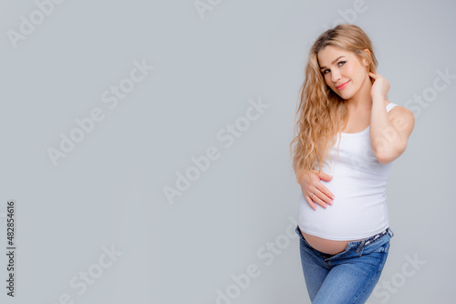 Concept Of A Happy Pregnancy. The Expectant Mother Touches Her Stomach, Smiling At The Camera Standing On A White Background. Studio shot © Olesya Pogosskaya