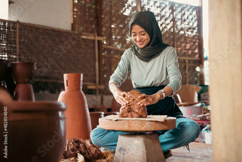 a veiled woman makes pottery on wheels in a studio