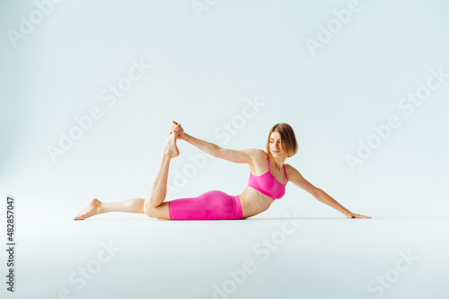 Attractive young woman in pink sportswear goes in for sports on a white cyclorama, doing stretch marks with a serious face.