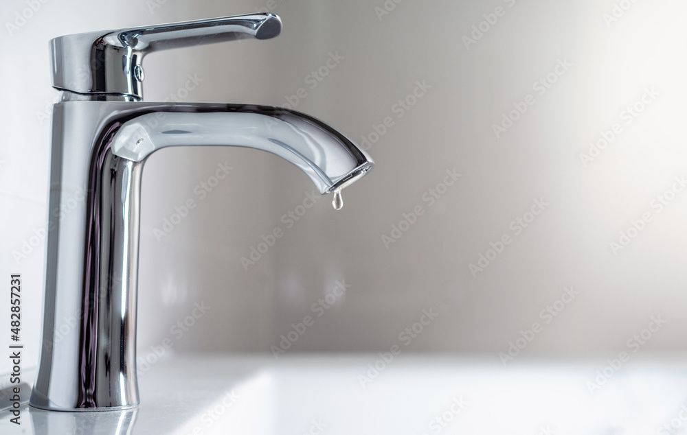 Faucet with a drop of water against a white sink. Water leaking and saving. Selective focus. Faucet with a drop of water against a white sink. Water leaking and saving. Selective focus.
