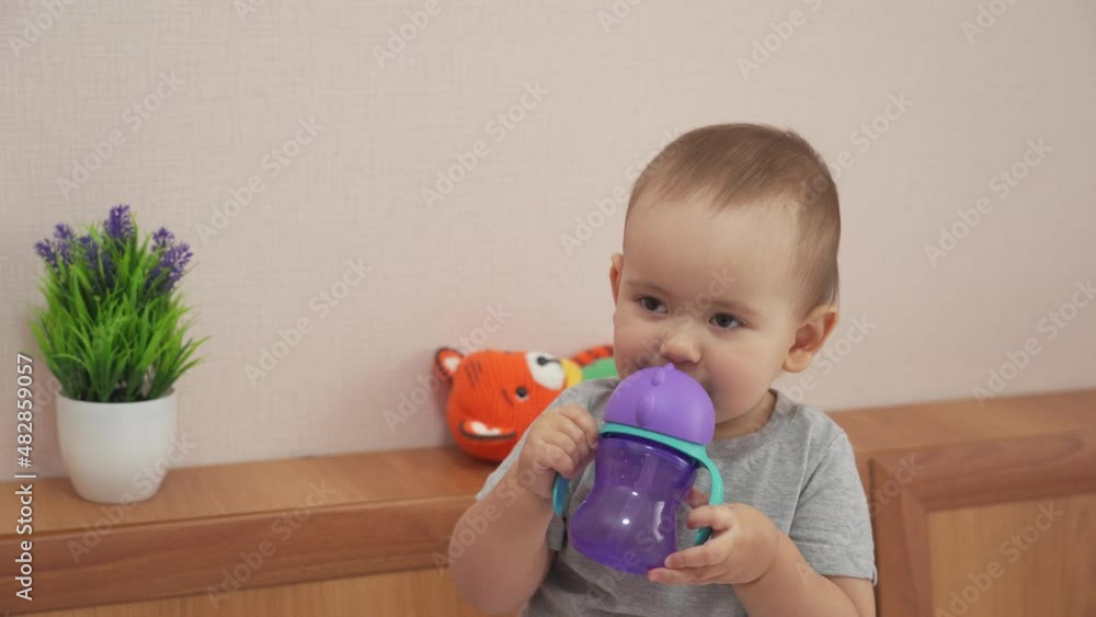 A newborn baby 12-17 months old drinks water from a baby plastic bottle and puts it away A newborn baby 12-17 months old drinks water from a baby plastic bottle and puts it away
