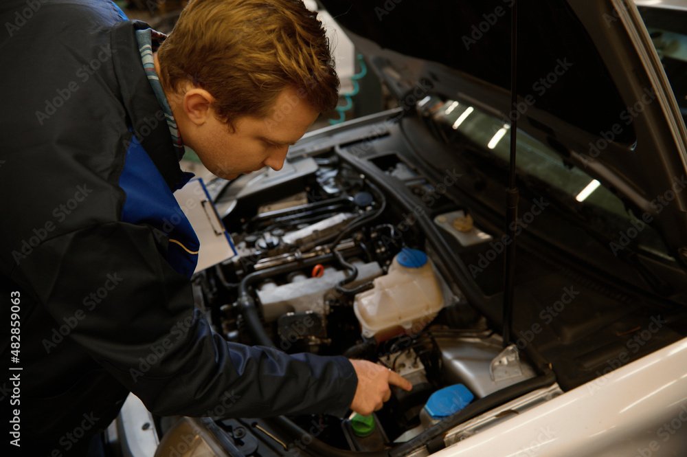 Overhead view of a mechanic inspecting the car under hood, examining the engine in a car repair workshop . Close-up Overhead view of a mechanic inspecting the car under hood, examining the engine in a car repair workshop . Close-up