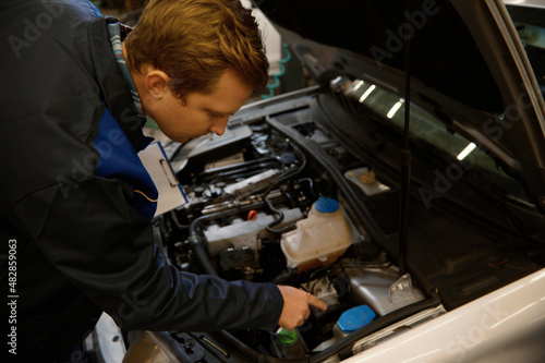 Overhead view of a mechanic inspecting the car under hood, examining the engine in a car repair workshop . Close-up