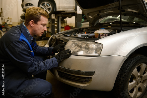 Auto mechanic in car service adjusting headlights on car in the repair shop garage. Auto service, car repair and warranty maintenance concept