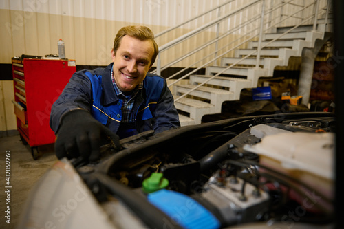 Handsome young Caucasian car engineer, technician mechanic in car service adjusting headlights on car in the repair shop garage. Auto service, car repair and warranty maintenance concept