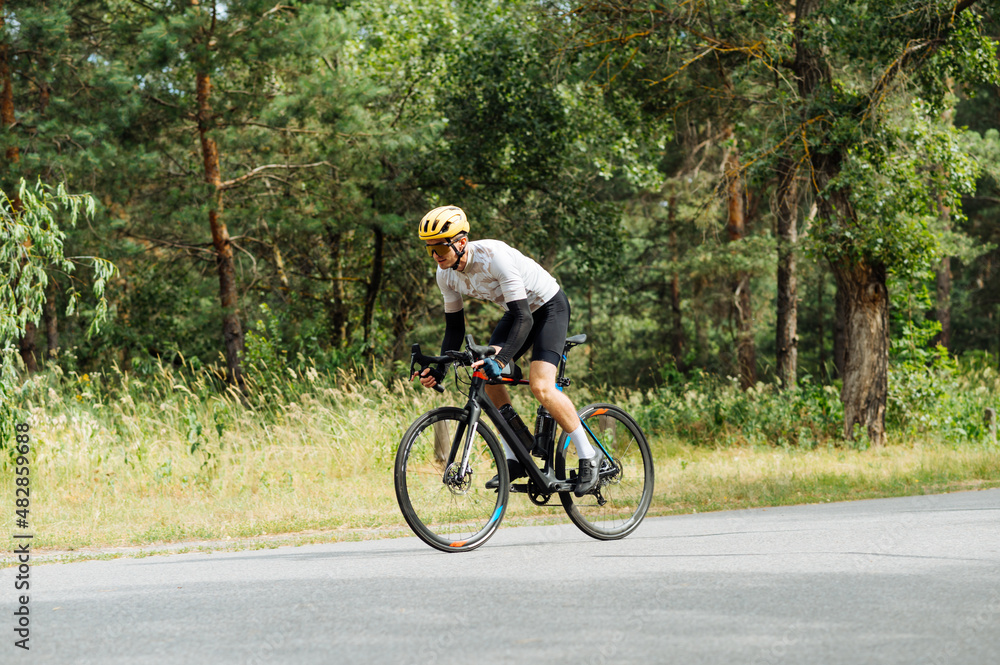Male cyclist rides a bicycle quickly on an asphalt road in the woods outdoors. The cyclist is training.