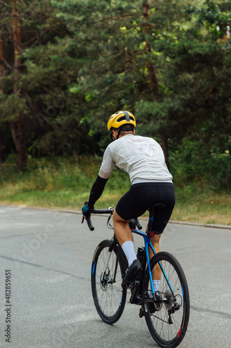 Male cyclist in outfit rides a bicycle in nature on an asphalt road through the woods.