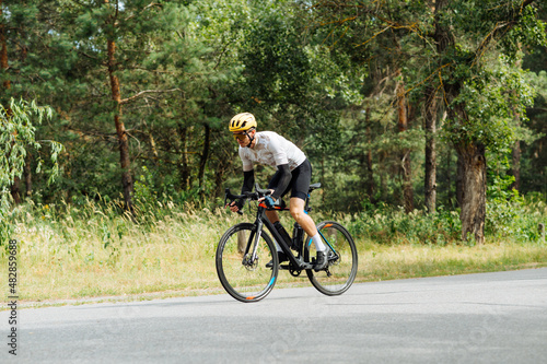 Male cyclist rides a bicycle quickly on an asphalt road in the woods outdoors. The cyclist is training.