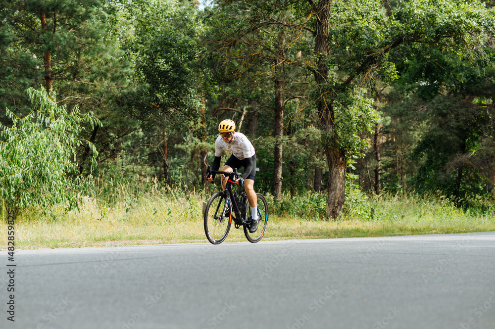 Athletic guy in sports outfit rides a bike on a forest road and trains.