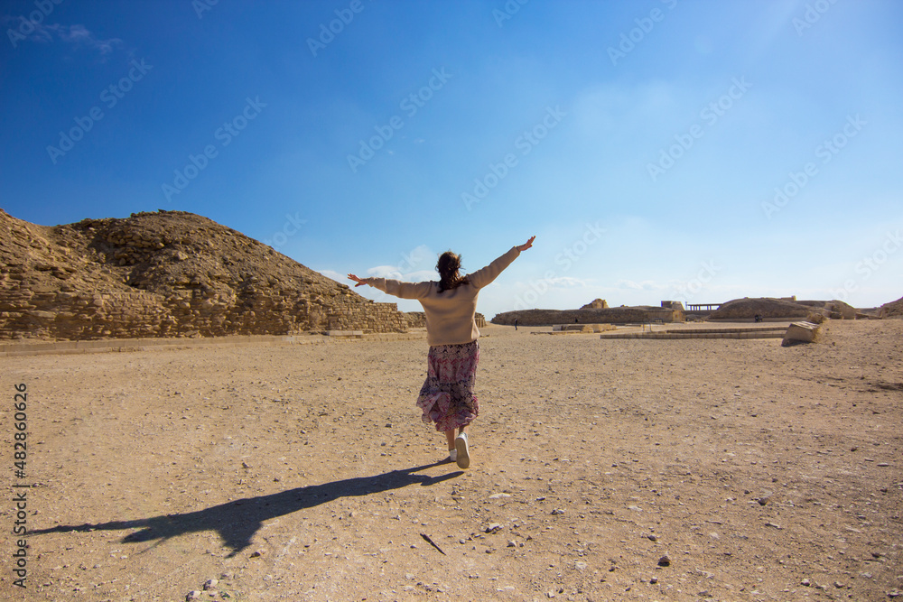Woman in dress is running and feeling freedom on the territory the complex of the Djoser Step Pyramid, Saqqara necropolis, south of Cairo, Egypt, Africa. I believe i can fly. Travel concept