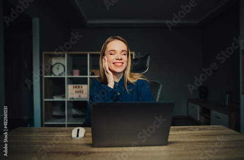 Smiling freelancer girl sitting at the table at home in a cozy apartment with a laptop and smiling. Happy lady working at home.