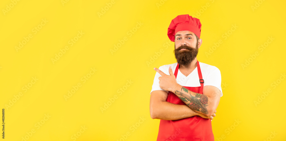 Man cook in toque and apron pointing finger aside yellow background copy space, advertise