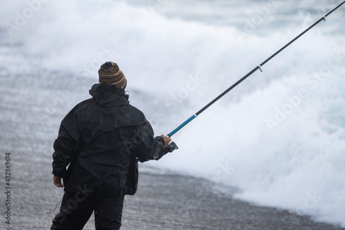 Unrecognizable man with a wool cap fishing on a cold and bad weather day