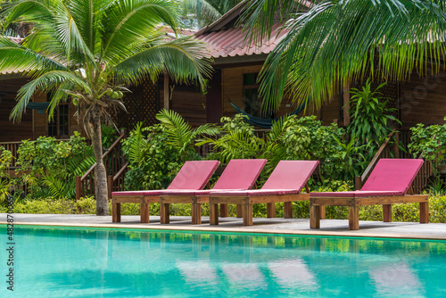 Swimming pool with relaxing beds and green palm trees in tropical garden , Thailand