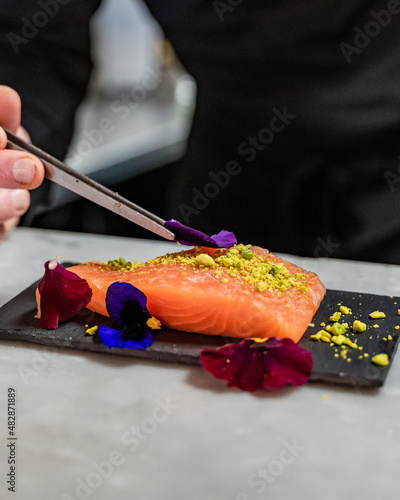 Un chef pose un pétale de fleur sur un morceau de saumon frais dans une cuisine