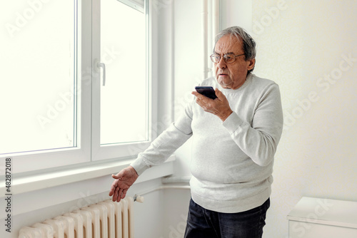 Cropped shot of an old men suffering cold at home and having problem with house heating, calling repair service for help. photo