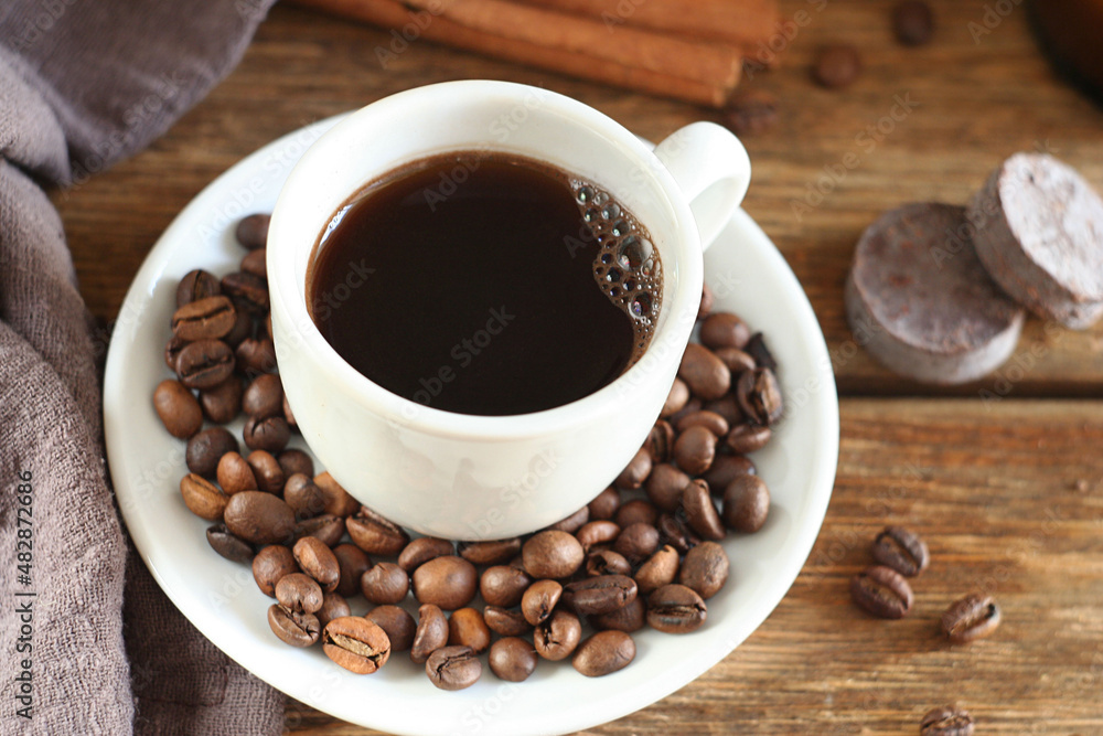 Freshly brewed coffee in a cup on a wooden table. Nearby are a towel, cinnamon, chocolate. Behind is a candle in a jar. Freshly brewed coffee in a cup on a wooden table. Nearby are a towel, cinnamon, chocolate. Behind is a candle in a jar.