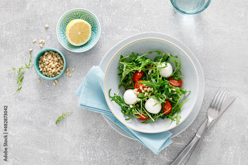 Fresh vegetable Caprese salad with arugula, tomato, pine nuts and mini mozzarella cheese. Top view Fresh vegetable Caprese salad with arugula, tomato, pine nuts and mini mozzarella cheese. Top view