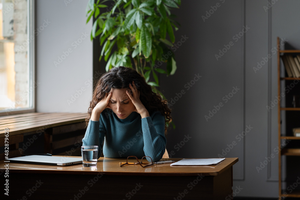 Exhausted stressed woman sitting at office desk with closed laptop tired of overwork, stress, problems and lack of inspiration. Female writer or student suffer from professional burnout at workplace - obrazy, fototapety, plakaty 