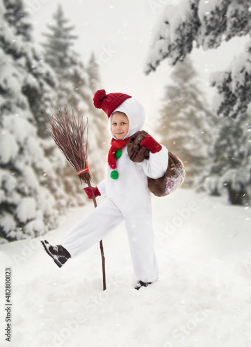 a small child in a snowman costume walks through the forest with a broom and gifts on the background of Christmas trees for the new year and Christmas