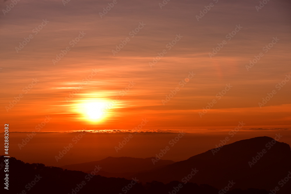 Obraz premium The sun set behind thick forests followed by mountains.