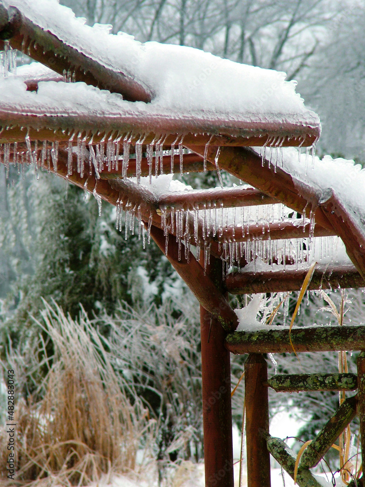 Vertical image of a large wooden garden arbor with icicles and snow in winter garden Vertical image of a large wooden garden arbor with icicles and snow in winter garden