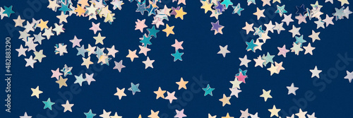 Festive background with holographic sparkling stars confetti on dark blue background. Christmas  New Year or birthday party background for your project. Banner