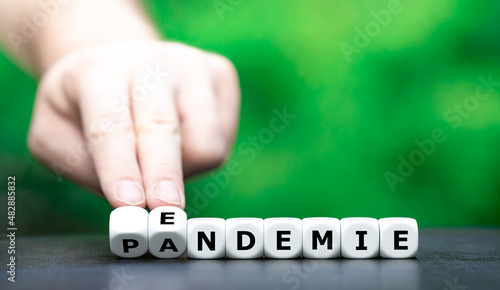 Symbol for a shift from pandemic to endemic. Hand turns dice and changes the German word "Pandemie" (pandemic) to "Endemie" (endemic).