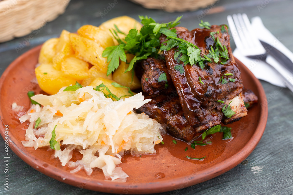 Bavarian pork ribs baked with sauce with boiled potatoes and sauerkraut