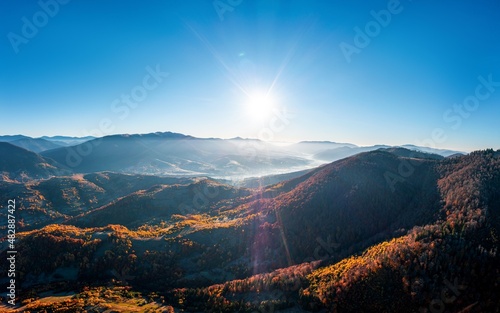 High mountain peaks with yellowed forest under bright sun