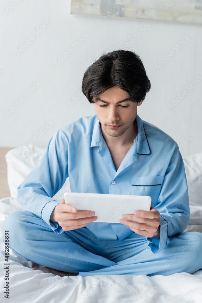 brunette man with digital tablet sitting with crossed legs on white bedding. brunette man with digital tablet sitting with crossed legs on white bedding.
