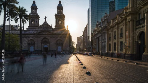 Zoom out time lapse view of sun setting behind historical landmark Santiago Metropolitan Cathedral at Plaza de Armas square in Downtown Santiago, the capital and largest city of Chile. photo