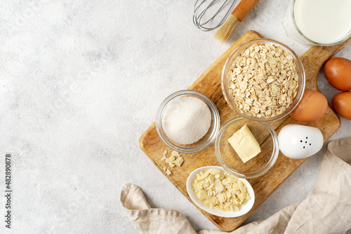 Ingredients for pudding or oatmeal pie on a light gray culinary background. Eggs, cereals, almonds, sugar, milk and butter on the kitchen table. Top view	
