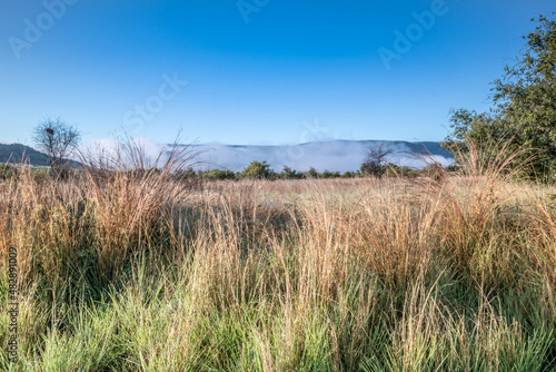 A wet Landscape view of mountains, brown and green savanna grassland covered in water drops and rain puddles after a rainstorm, Pilanesburg Nature Reserve, North West Province, South Africa