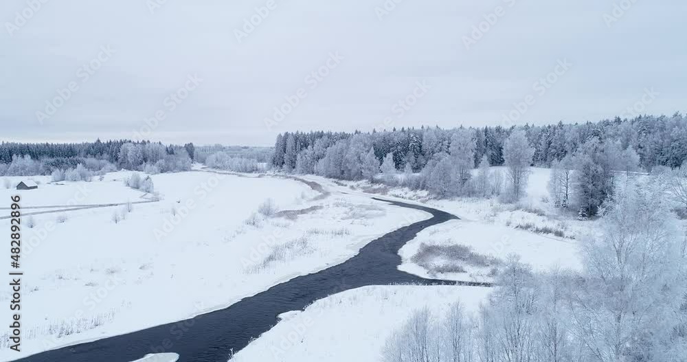 Moving backwards above a frosty and snowy rural landscape with a open river in Estonian winter, Northern Europe. Moving backwards above a frosty and snowy rural landscape with a open river in Estonian winter, Northern Europe.