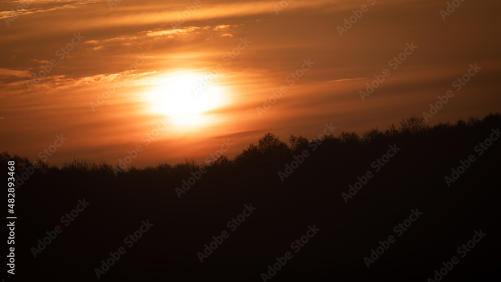 Beautiful wild sunrise over the forest and orange cloudy sky. The sun behind the clouds
