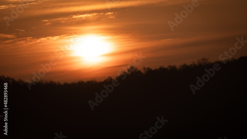 Beautiful wild sunrise over the forest and orange cloudy sky. The sun behind the clouds