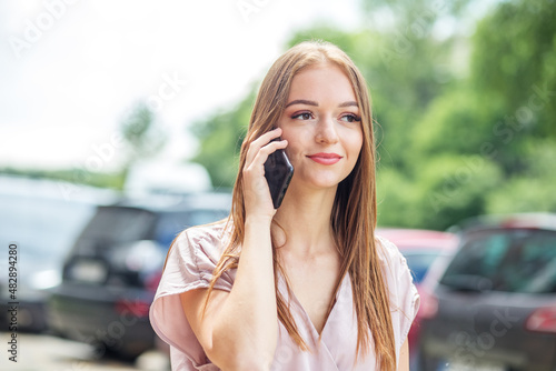 Cheerful adult woman talking on mobile phone. Walk around city on summer day.