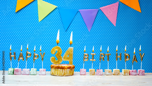 Congratulations on your birthday from the letters of candles number 34 on a blue background with polka dots white copy space. Happy birthday muffin with burning golden color candle for thirty four. photo