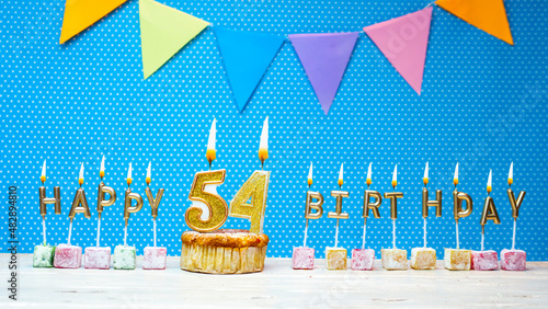 Congratulations on your birthday from the letters of the candles number 54 on a blue background with polka dots white copy space. Happy birthday muffin with burning golden color candle for fifty four  photo
