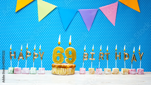 Happy birthday from number 69 candle letters on a blue background with white polka dot copy space. Happy birthday cupcake with burning golden candle for sixty nine years old photo
