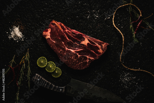 corte de res  AGUJA NORTEÑA  sobre laja de piedra  con decoración como sal, pimienta limón, chile de árbol  , romero y un cuchillo  