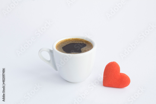 Close-up on coffee cup and red heart shaped cookie on the white background. Copy space.