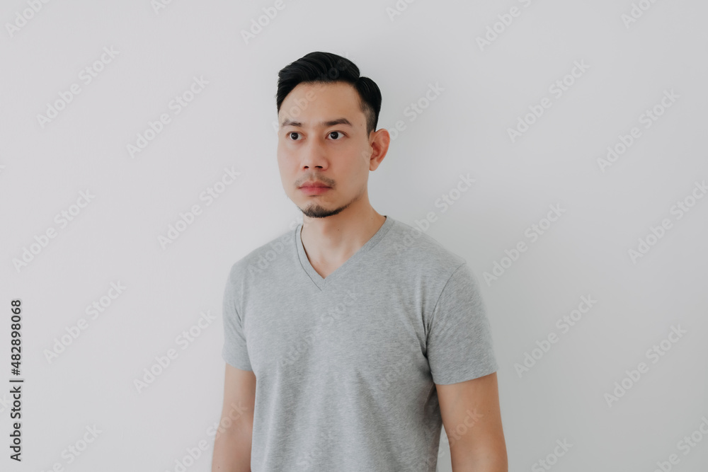 Straight face portrait of serious Asian man in grey t-shirt on white wall. Straight face portrait of serious Asian man in grey t-shirt on white wall.