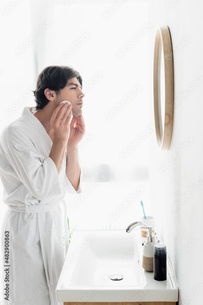 side view of man in white bathrobe cleaning face with cotton pad in bathroom. side view of man in white bathrobe cleaning face with cotton pad in bathroom.