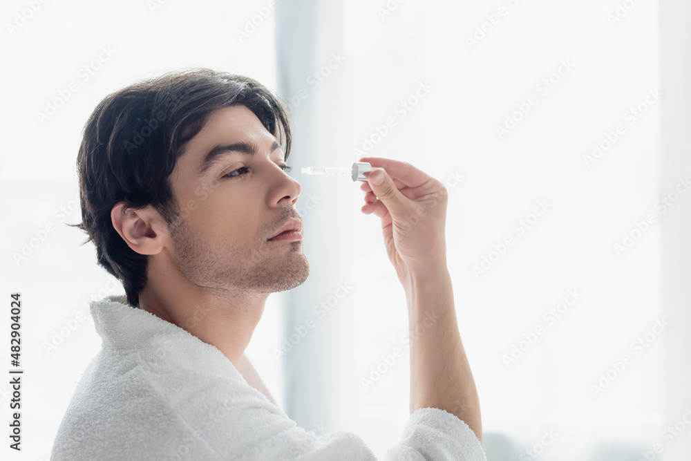 young man in white bathrobe applying cosmetic serum in bathroom. young man in white bathrobe applying cosmetic serum in bathroom.
