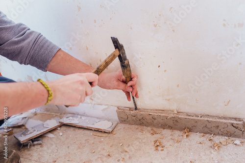 Person removing the skirting board with a hammer and chisel.