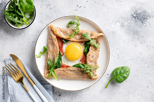 French buckwheat crepe with egg, ham and spinach on gray background. galette bretonne. flat lay with copy space photo