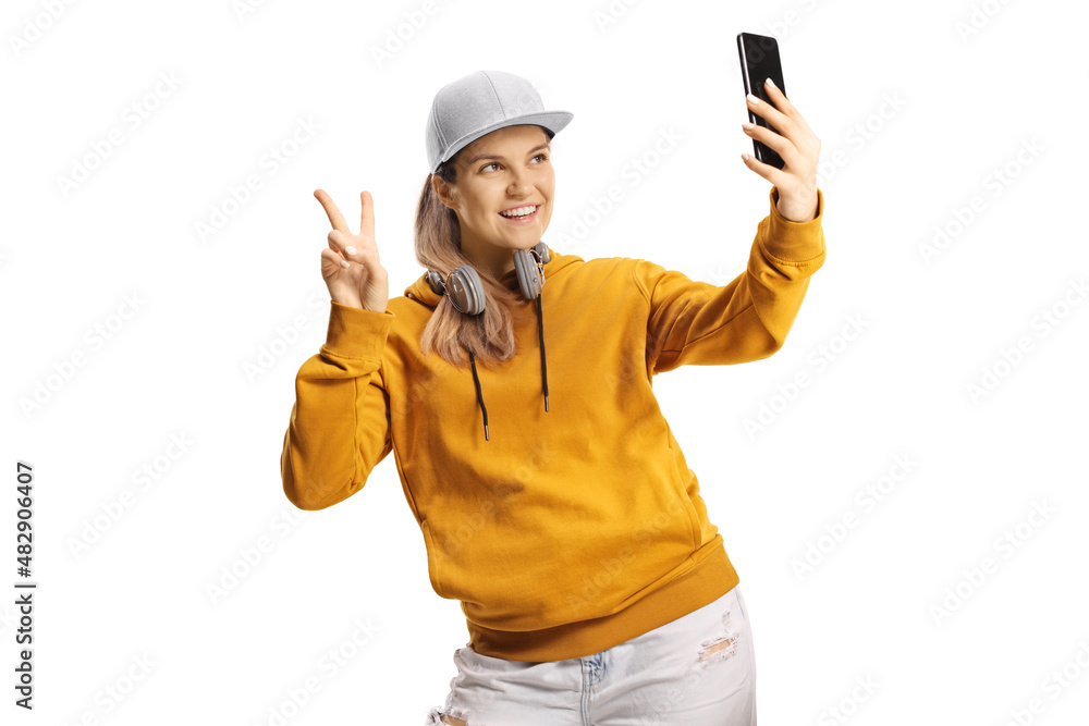 Young female with headphones taking a selfie with a smartphone and gesturing a victory sign Young female with headphones taking a selfie with a smartphone and gesturing a victory sign